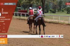 Live horse race scene: two jockeys on brown horses ride a dirt track; Riverside is shown as entrant with riders and stats on a red sidebar; départ timer 05:45 at bottom.