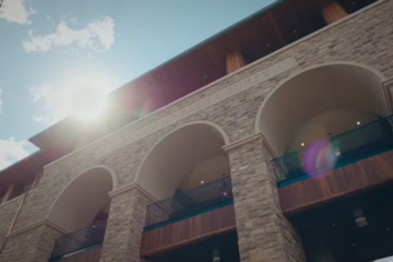 Stone building with large arched entryways and balconies under a bright, sunlit sky.